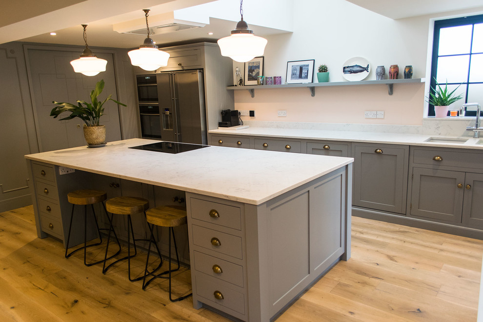 Large contemporary l-shaped open plan kitchen in Surrey with flat-panel cabinets, quartz worktops, an island, white worktops and grey cabinets.