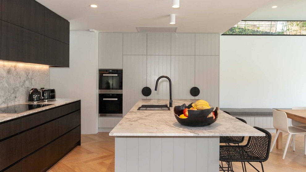 Idéer för att renovera ett stort funkis grå grått kök, med en undermonterad diskho, grå skåp, bänkskiva i kvartsit, grått stänkskydd, stänkskydd i sten, svarta vitvaror, ljust trägolv, en köksö och beiget golv