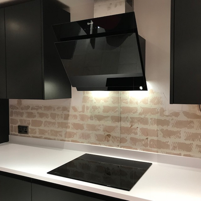 Medium sized modern galley open plan kitchen in Cambridgeshire with flat-panel cabinets, black cabinets, composite countertops, black appliances, no island and white worktops.