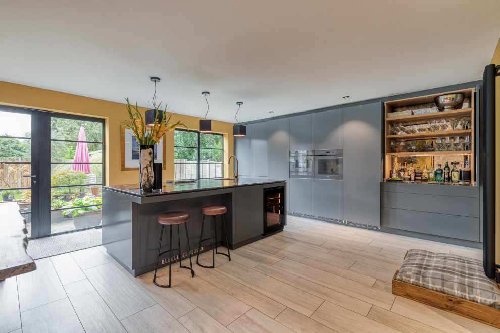 Inspiration for a large contemporary l-shaped eat-in kitchen remodel in Hertfordshire with a drop-in sink, flat-panel cabinets, gray cabinets, granite countertops, paneled appliances, an island and black countertops
