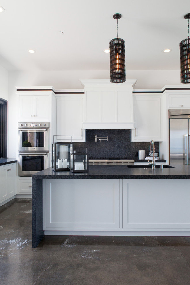 Exempel på ett modernt kök med öppen planlösning, med en undermonterad diskho, luckor med infälld panel, vita skåp, svart stänkskydd, stänkskydd i glaskakel, rostfria vitvaror, betonggolv och en köksö