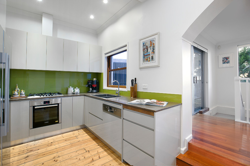Photo of a traditional u-shaped kitchen/diner in Sydney with a submerged sink, flat-panel cabinets, grey cabinets, green splashback, porcelain splashback, stainless steel appliances, light hardwood flooring and no island.