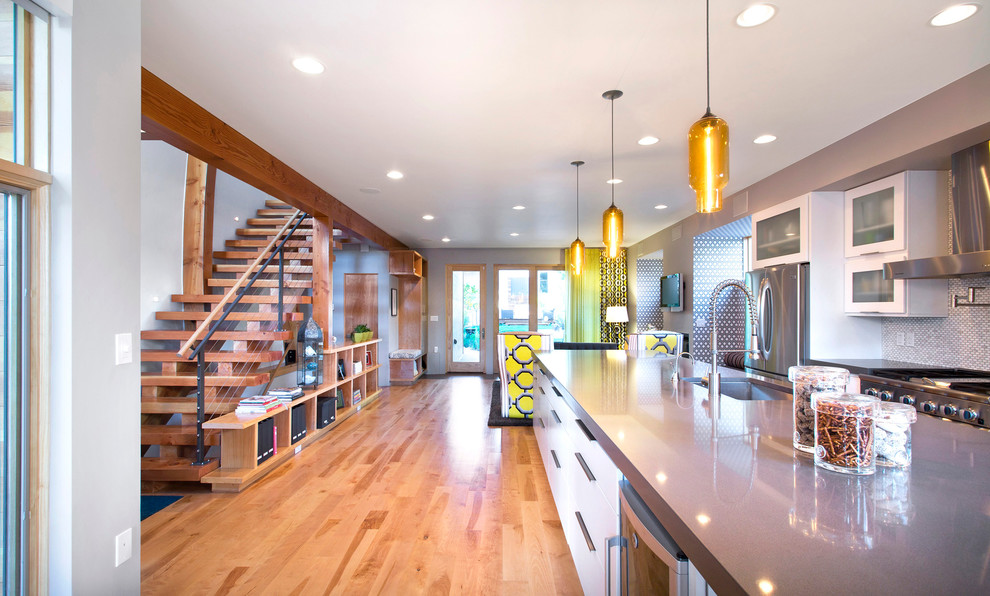 Example of a mid-sized trendy galley medium tone wood floor eat-in kitchen design in Denver with an undermount sink, glass-front cabinets, white cabinets, white backsplash, stainless steel appliances, ceramic backsplash and an island