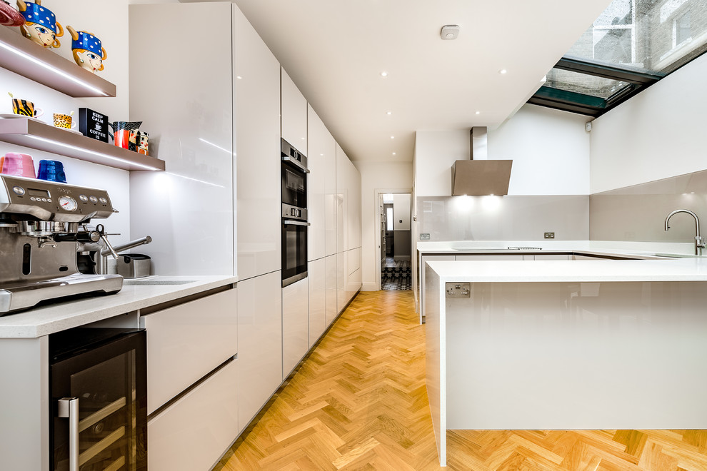 Design ideas for a large galley kitchen in London with a double-bowl sink, quartz worktops, glass sheet splashback, stainless steel appliances, light hardwood flooring, a breakfast bar, yellow floors and white worktops.