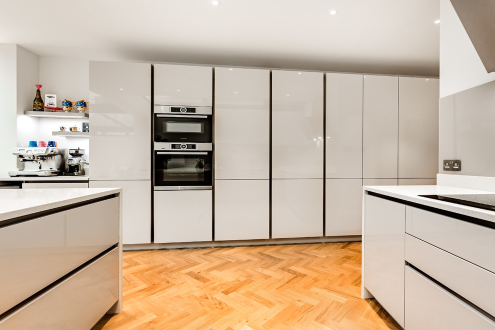 ロンドンにある低価格の広いおしゃれなキッチン (ダブルシンク、珪岩カウンター、ガラス板のキッチンパネル、シルバーの調理設備、淡色無垢フローリング、黄色い床、白いキッチンカウンター) の写真