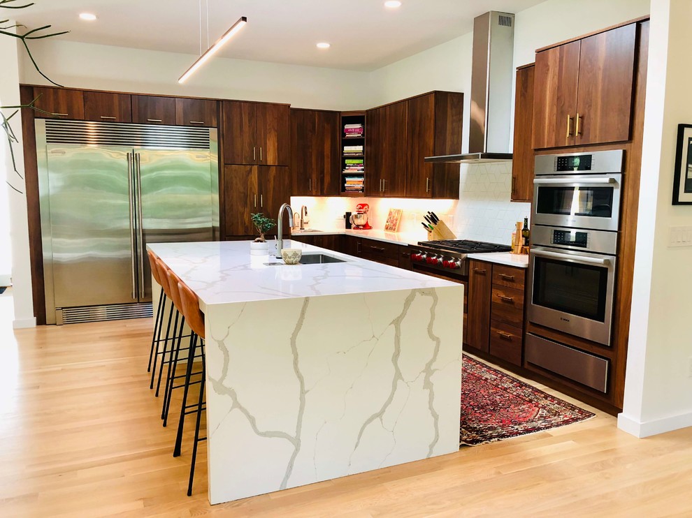 Design ideas for a contemporary single-wall kitchen in Raleigh with a submerged sink, flat-panel cabinets, dark wood cabinets, white splashback, stainless steel appliances, light hardwood flooring, an island, beige floors and white worktops.