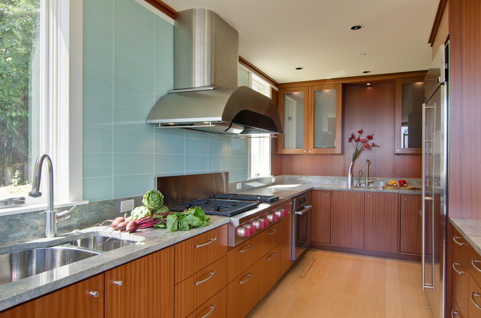 Design ideas for a medium sized modern l-shaped enclosed kitchen in Portland with a submerged sink, flat-panel cabinets, light wood cabinets, engineered stone countertops, green splashback, glass sheet splashback, stainless steel appliances, light hardwood flooring, an island and beige floors.