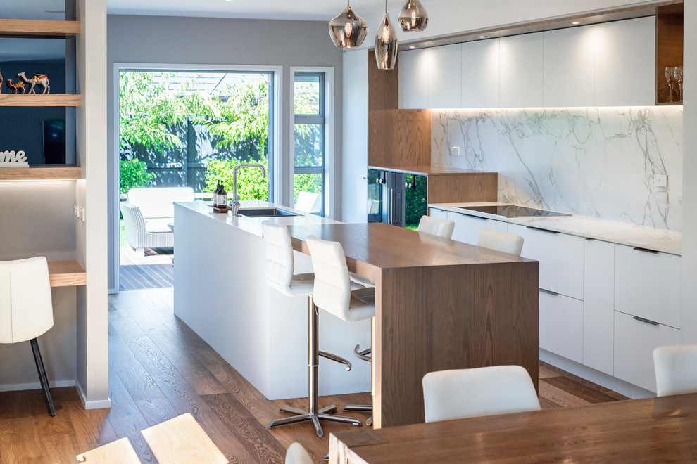 Photo of a medium sized contemporary galley kitchen/diner in Christchurch with white splashback, marble splashback, light hardwood flooring, an island, brown floors and white worktops.