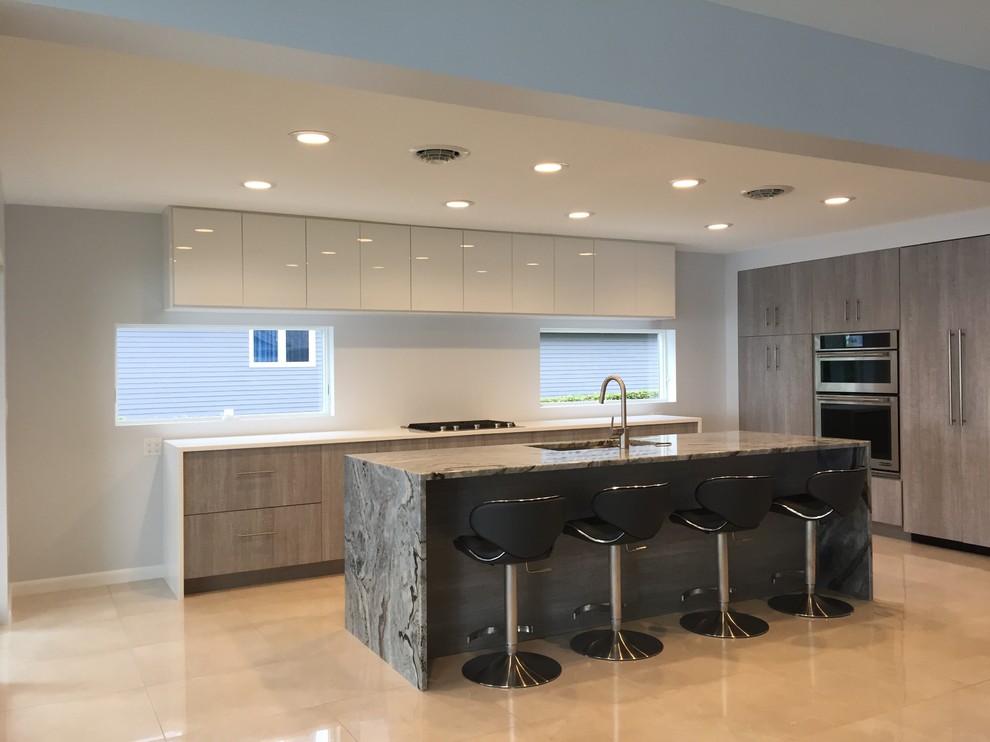 Example of a large minimalist l-shaped limestone floor and beige floor open concept kitchen design in Burlington with an undermount sink, flat-panel cabinets, light wood cabinets, granite countertops, white backsplash, paneled appliances and an island