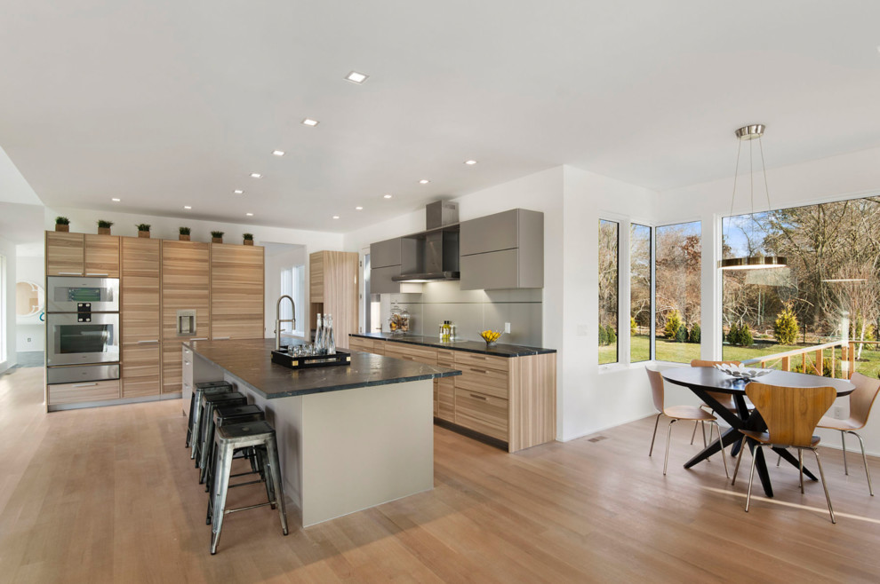 Cette image montre une cuisine design en L et bois clair avec un placard à porte plane, un électroménager en acier inoxydable, un sol en bois brun, îlot et un sol marron.