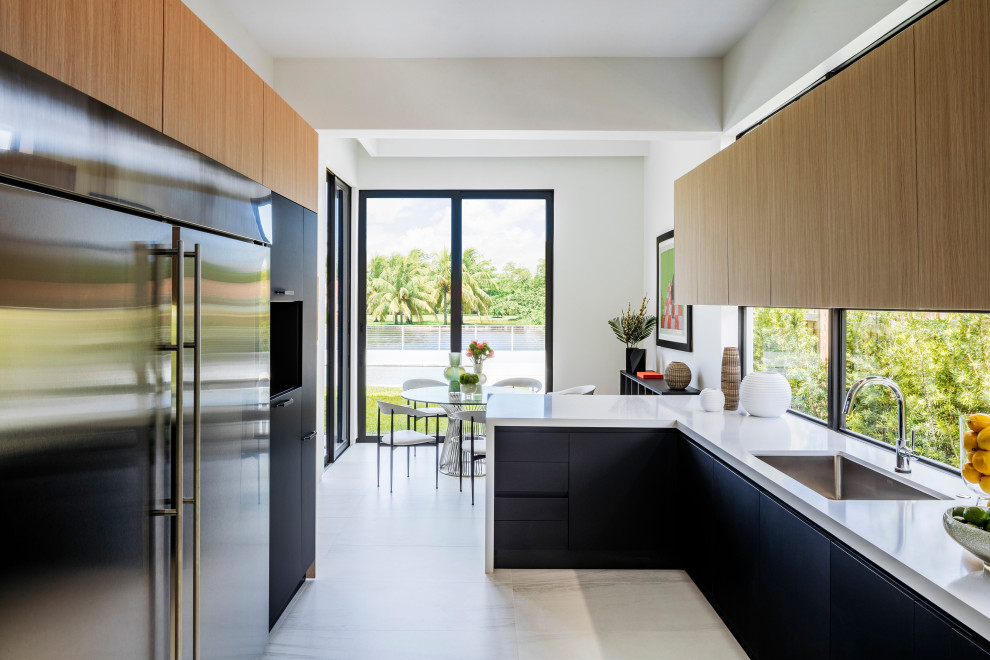 Photo of a modern galley kitchen/diner in Miami with a submerged sink, light wood cabinets, stainless steel appliances, marble flooring, a breakfast bar, white floors and white worktops.