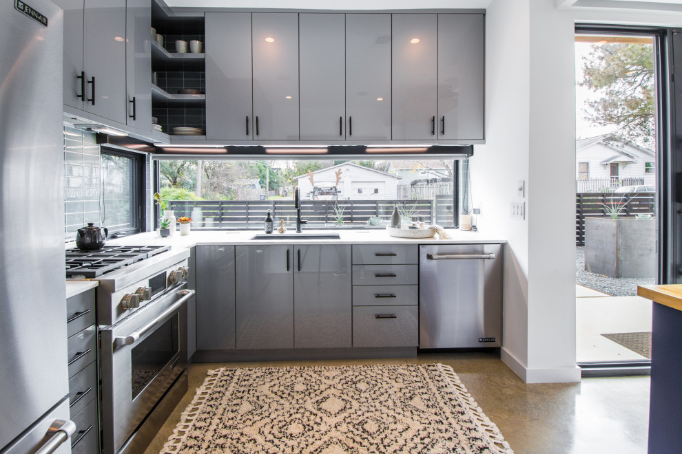 Trendy l-shaped concrete floor and gray floor kitchen photo in Austin with an undermount sink, flat-panel cabinets, gray cabinets, window backsplash, stainless steel appliances, an island and white countertops