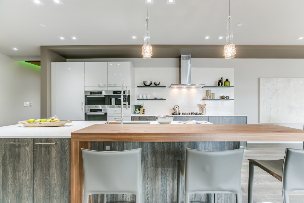Inspiration for a large contemporary galley light wood floor and gray floor eat-in kitchen remodel in Seattle with an island, an undermount sink, flat-panel cabinets, white cabinets, white backsplash, stainless steel appliances and white countertops