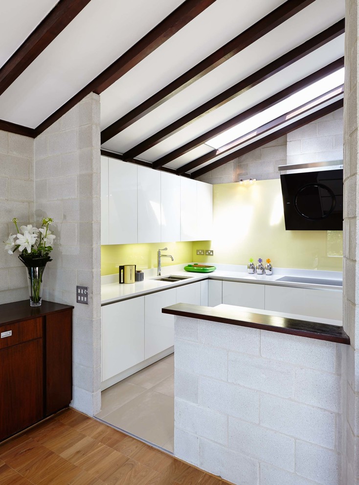 Photo of a large contemporary u-shaped open plan kitchen in Hampshire with a submerged sink, flat-panel cabinets, white cabinets, composite countertops, yellow splashback, glass sheet splashback, stainless steel appliances, no island and porcelain flooring.