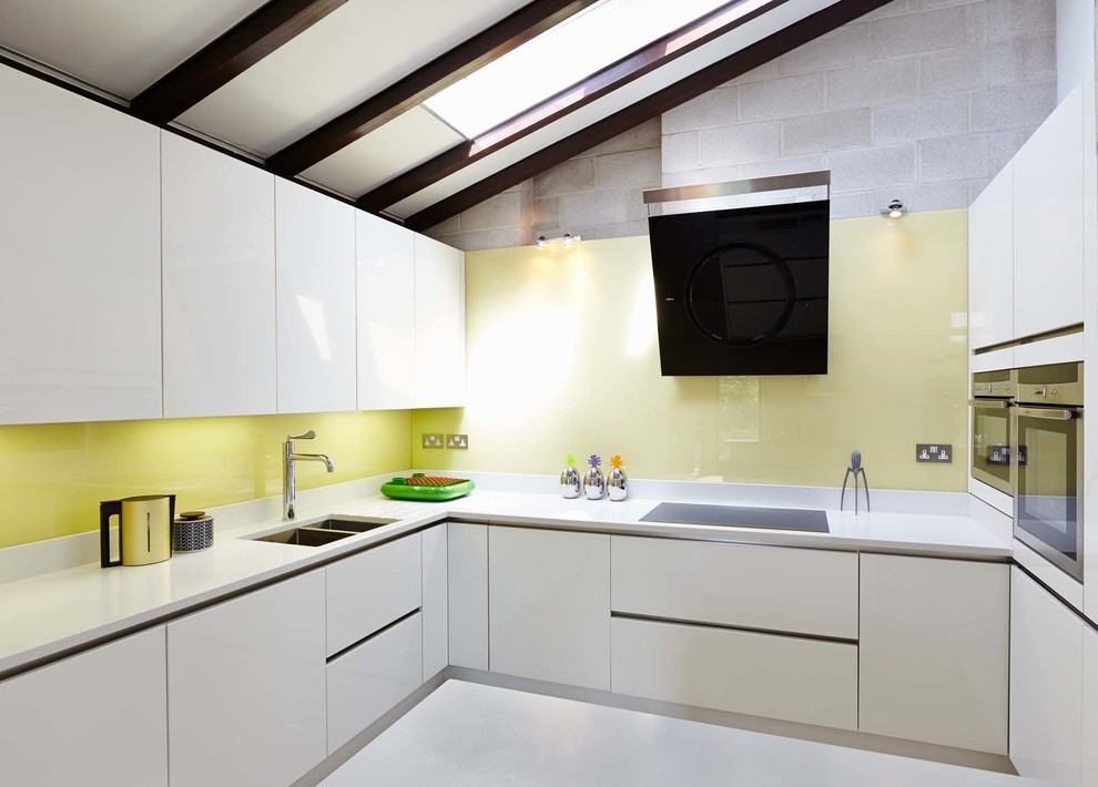 Design ideas for a large contemporary u-shaped open plan kitchen in Hampshire with a submerged sink, flat-panel cabinets, white cabinets, composite countertops, yellow splashback, glass sheet splashback, stainless steel appliances, porcelain flooring and no island.