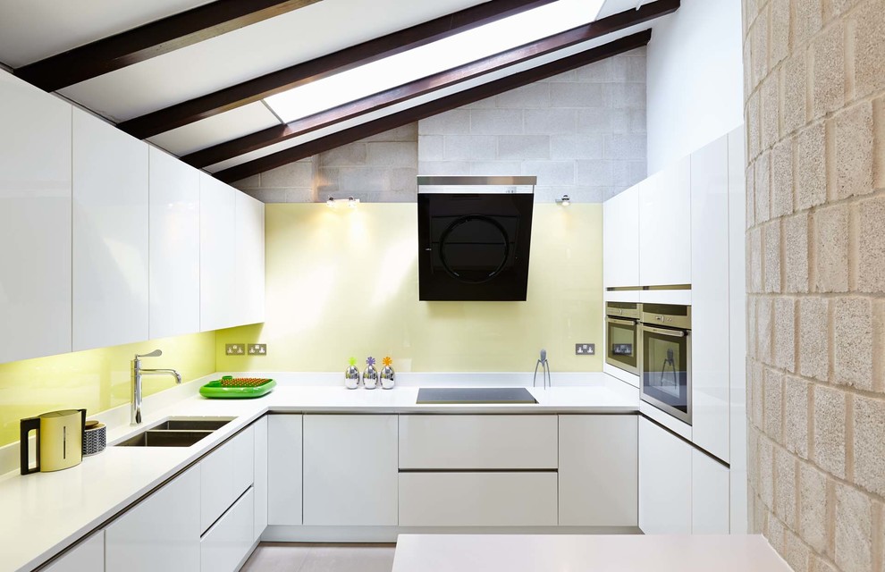 Photo of a large contemporary u-shaped open plan kitchen in Hampshire with a submerged sink, flat-panel cabinets, white cabinets, composite countertops, yellow splashback, glass sheet splashback, stainless steel appliances, no island and porcelain flooring.
