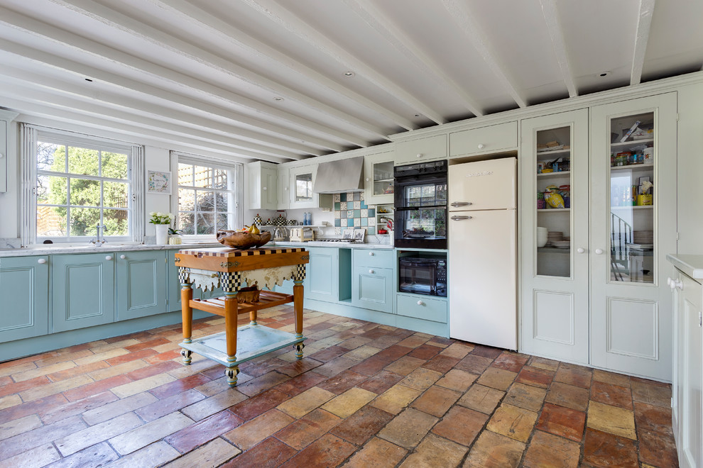 ロンドンにある中くらいなシャビーシック調のおしゃれなキッチン (落し込みパネル扉のキャビネット、青いキャビネット、大理石カウンター、マルチカラーのキッチンパネル、モザイクタイルのキッチンパネル、パネルと同色の調理設備、テラコッタタイルの床、茶色い床) の写真
