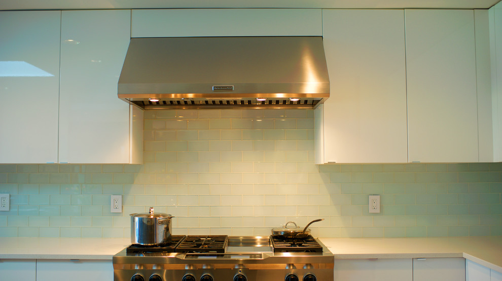 Bild på ett stort funkis kök, med vita skåp, blått stänkskydd, rostfria vitvaror, ljust trägolv och en köksö