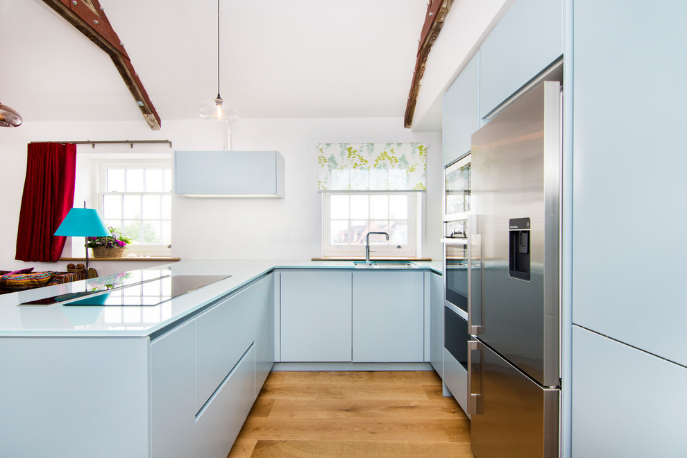 Offene, Zweizeilige, Kleine Moderne Küche mit flächenbündigen Schrankfronten, blauen Schränken, Glas-Arbeitsplatte, Küchengeräten aus Edelstahl, Waschbecken und braunem Holzboden in Essex