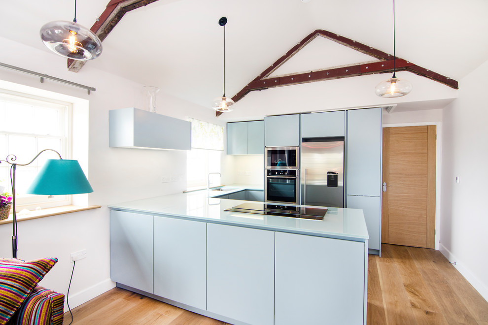 Bild på ett litet funkis kök, med släta luckor, blå skåp, bänkskiva i glas, rostfria vitvaror, en enkel diskho, mellanmörkt trägolv och brunt golv