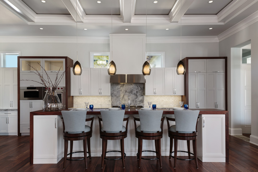 Klassische Küche mit Schrankfronten mit vertiefter Füllung, weißen Schränken, Arbeitsplatte aus Holz, Küchenrückwand in Grau, Rückwand aus Marmor, Küchengeräten aus Edelstahl, dunklem Holzboden, Kücheninsel und braunem Boden in Miami