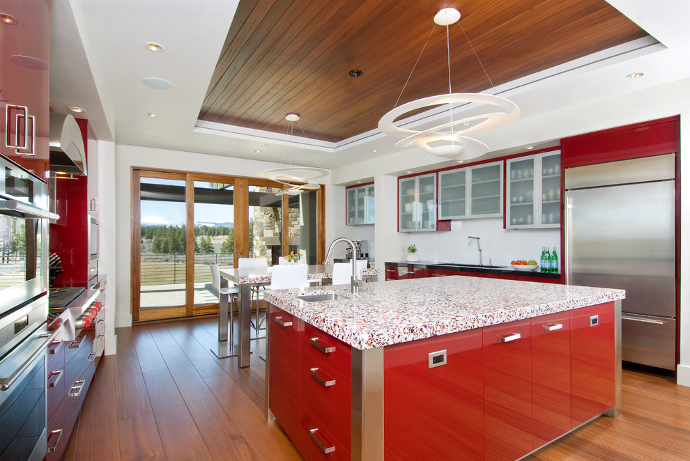 他の地域にあるコンテンポラリースタイルのおしゃれなキッチン (赤いキャビネット、フラットパネル扉のキャビネット、シルバーの調理設備、赤いキッチンカウンター) の写真