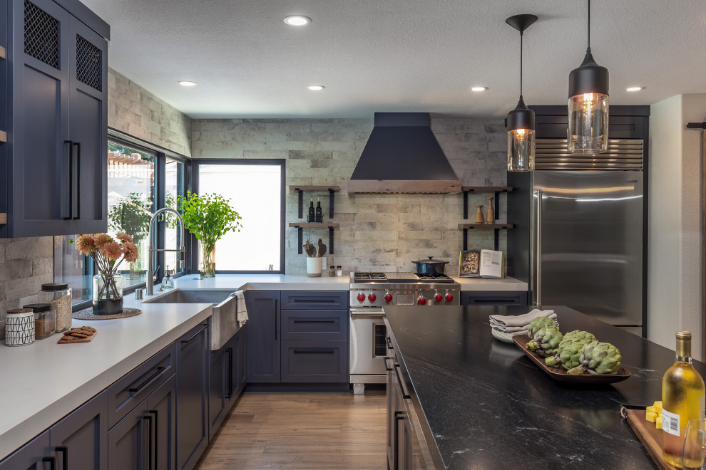 Photo of a large industrial l-shaped kitchen/diner in San Francisco with a submerged sink, shaker cabinets, black cabinets, granite worktops, stone slab splashback, stainless steel appliances, laminate floors, an island, brown floors and black worktops.