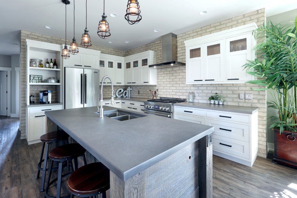 Industriell inredning av ett kök, med en undermonterad diskho, luckor med infälld panel, vita skåp, bänkskiva i betong, rostfria vitvaror, mörkt trägolv och en köksö