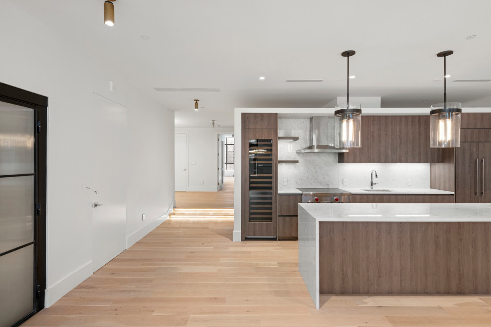 Design ideas for a medium sized modern galley kitchen/diner in New York with a submerged sink, flat-panel cabinets, brown cabinets, marble worktops, white splashback, marble splashback, stainless steel appliances, light hardwood flooring, an island, multi-coloured floors and white worktops.