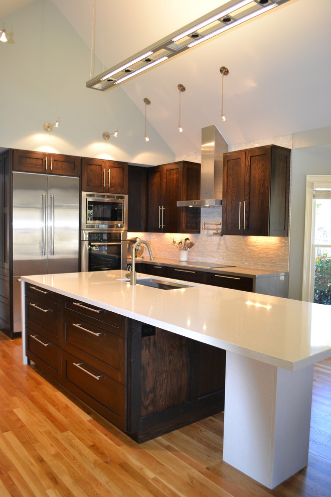 Large minimalist l-shaped medium tone wood floor and brown floor enclosed kitchen photo in Atlanta with stainless steel appliances, an undermount sink, shaker cabinets, dark wood cabinets, quartz countertops, glass tile backsplash, an island and white backsplash