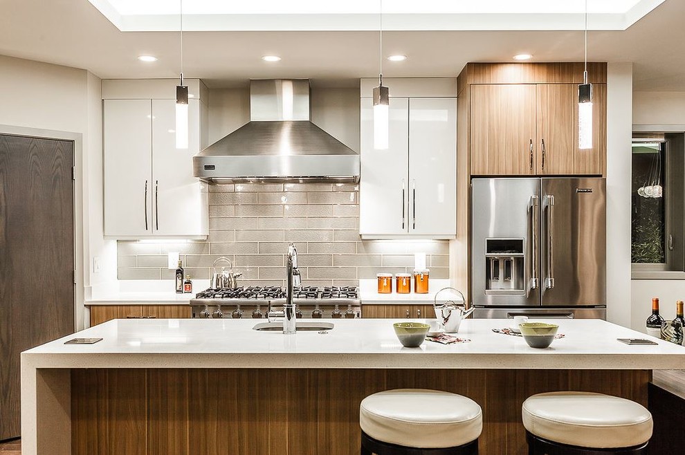Cette photo montre une cuisine parallèle tendance en bois brun avec un évier encastré, un placard à porte plane, une crédence grise, un électroménager en acier inoxydable et îlot.