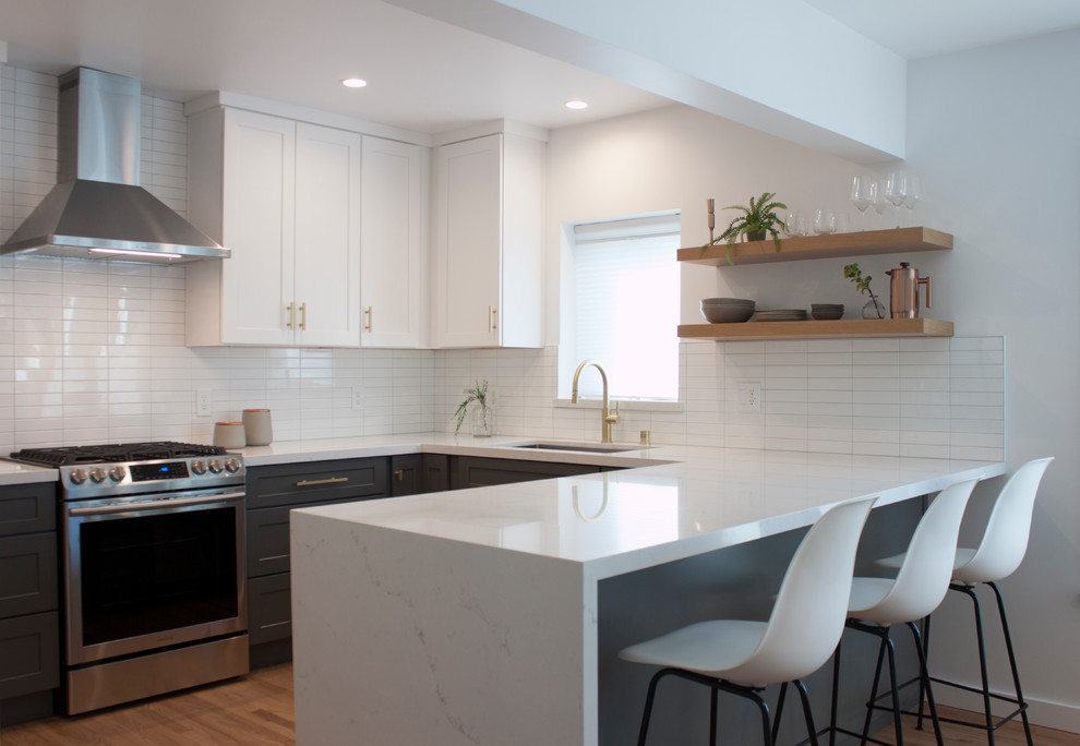 Photo of a traditional u-shaped kitchen in Los Angeles with a submerged sink, shaker cabinets, grey cabinets, white splashback, stainless steel appliances, medium hardwood flooring, a breakfast bar, brown floors and white worktops.