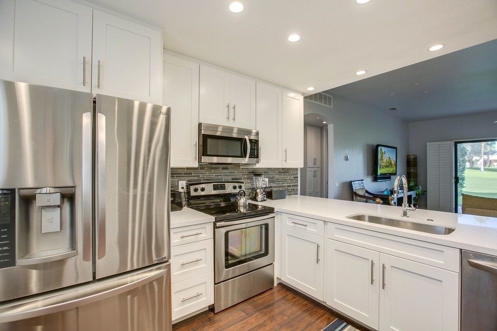 Exempel på ett litet klassiskt vit vitt kök, med en undermonterad diskho, skåp i shakerstil, vita skåp, bänkskiva i kvarts, brunt stänkskydd, stänkskydd i stickkakel, rostfria vitvaror, mellanmörkt trägolv, en halv köksö och brunt golv