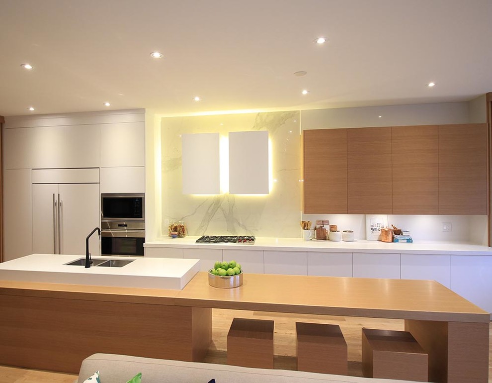 Immagine di una cucina moderna con lavello sottopiano, ante lisce, ante in legno chiaro, top in quarzo composito, paraspruzzi bianco, elettrodomestici in acciaio inossidabile, pavimento in laminato, pavimento beige e top bianco
