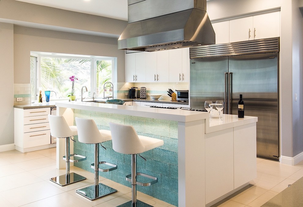 Photo of a large contemporary l-shaped kitchen/diner in Los Angeles with a submerged sink, flat-panel cabinets, white cabinets, composite countertops, white splashback, metro tiled splashback, stainless steel appliances, ceramic flooring and an island.