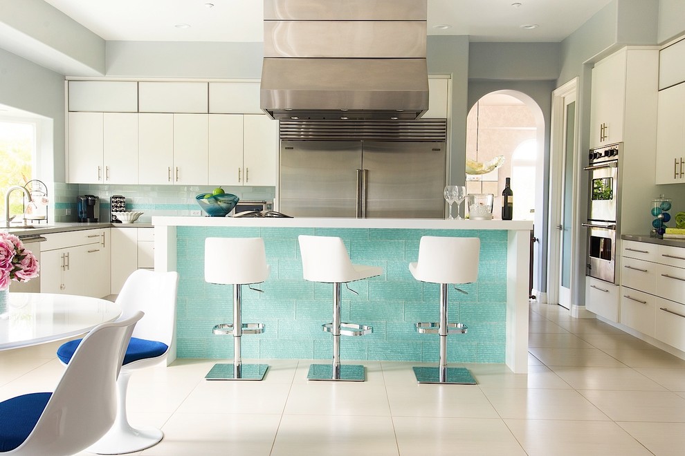 Photo of a large contemporary l-shaped kitchen/diner in Los Angeles with a submerged sink, flat-panel cabinets, white cabinets, composite countertops, white splashback, metro tiled splashback, stainless steel appliances, ceramic flooring and an island.