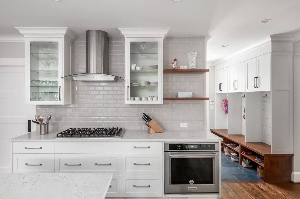 Modern inredning av ett stort vit vitt kök och matrum, med en undermonterad diskho, skåp i shakerstil, vita skåp, bänkskiva i kvarts, grått stänkskydd, stänkskydd i tunnelbanekakel, rostfria vitvaror, mörkt trägolv och en köksö