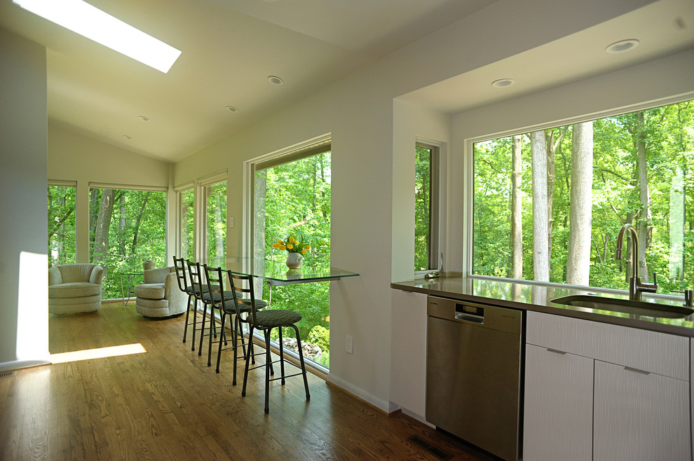 Example of a mid-sized trendy l-shaped light wood floor eat-in kitchen design in Baltimore with a single-bowl sink, flat-panel cabinets, white cabinets, quartz countertops, white backsplash, glass tile backsplash and stainless steel appliances