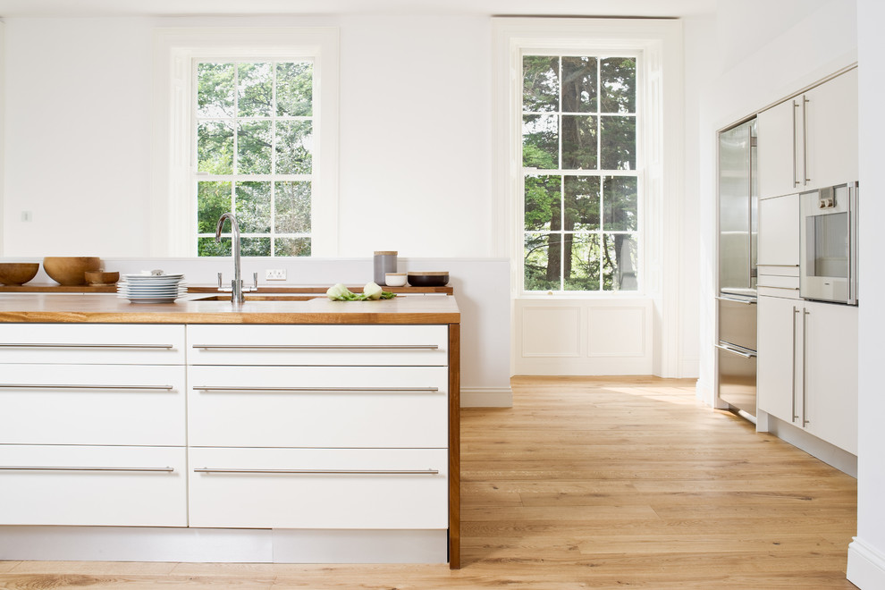 Moderne Küche mit flächenbündigen Schrankfronten, Küchengeräten aus Edelstahl, Arbeitsplatte aus Holz und weißen Schränken in Sonstige