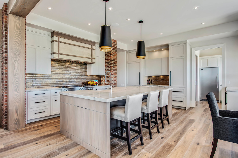 This is an example of a traditional l-shaped kitchen/diner in Calgary with a belfast sink, recessed-panel cabinets, white cabinets, multi-coloured splashback, metro tiled splashback, stainless steel appliances, light hardwood flooring, an island and white worktops.