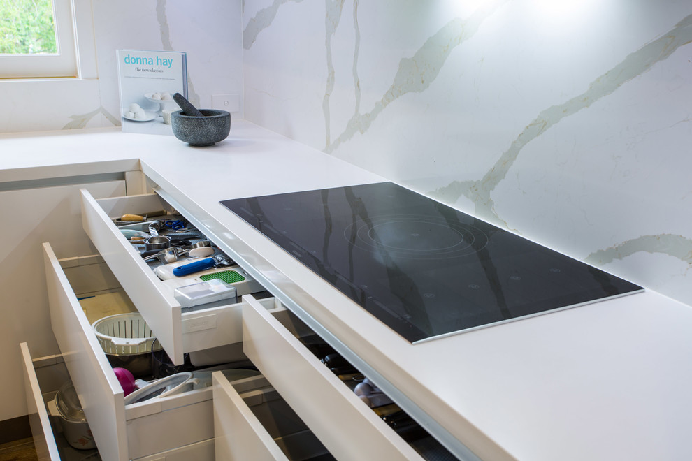 This is an example of an expansive contemporary u-shaped kitchen pantry in Brisbane with a single-bowl sink, flat-panel cabinets, white cabinets, engineered stone countertops, white splashback, stone slab splashback, stainless steel appliances, light hardwood flooring and an island.