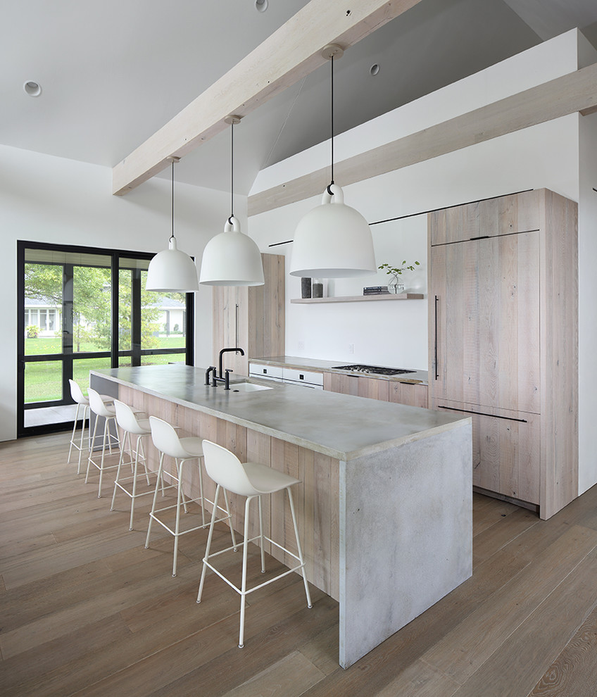 Modern galley kitchen in Milwaukee with light wood cabinets, concrete worktops, an island, a submerged sink, flat-panel cabinets, integrated appliances, medium hardwood flooring, brown floors and grey worktops.