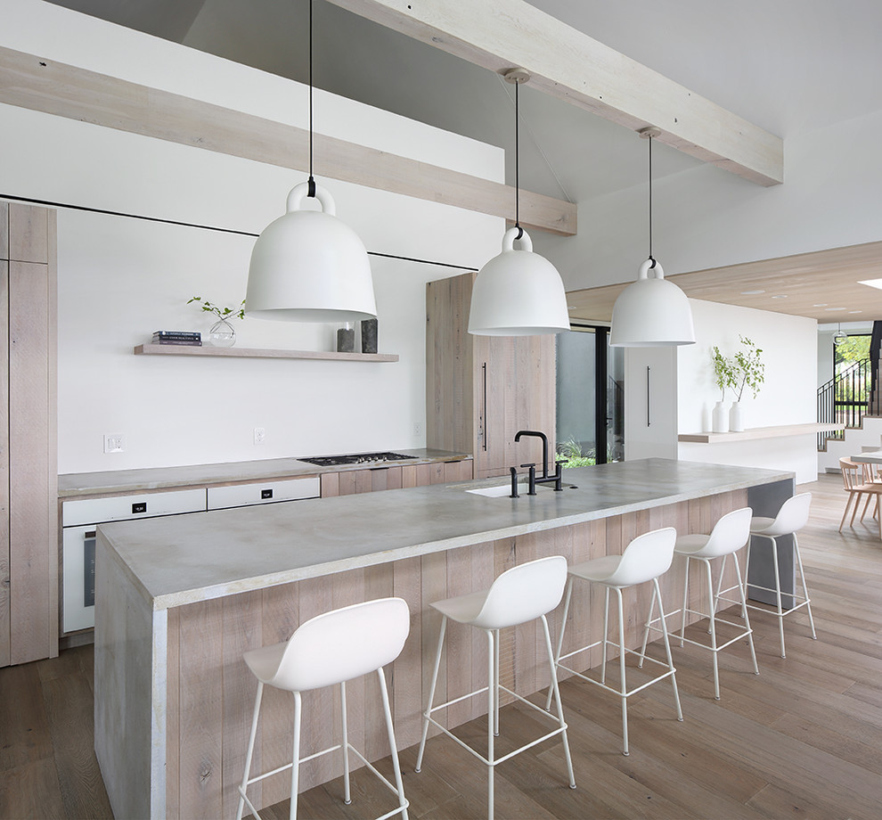 Foto di un cucina con isola centrale minimalista con ante in legno chiaro, top in cemento e parquet chiaro