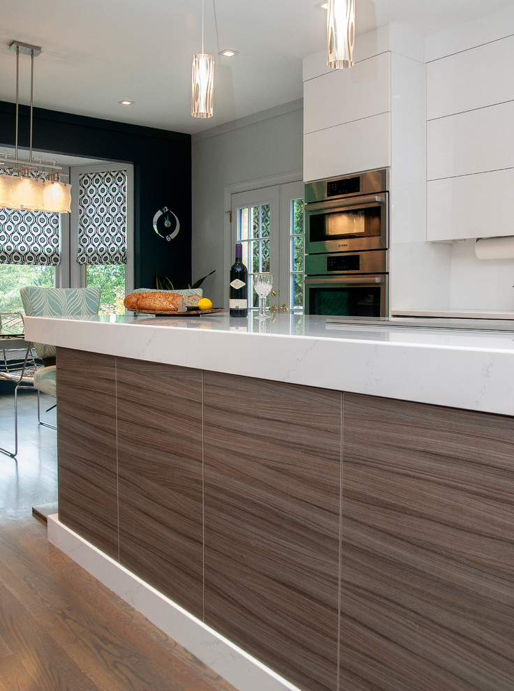 Aménagement d'une cuisine moderne avec des portes de placard blanches, un plan de travail en quartz, une crédence blanche, un électroménager en acier inoxydable, un sol en bois brun et îlot.