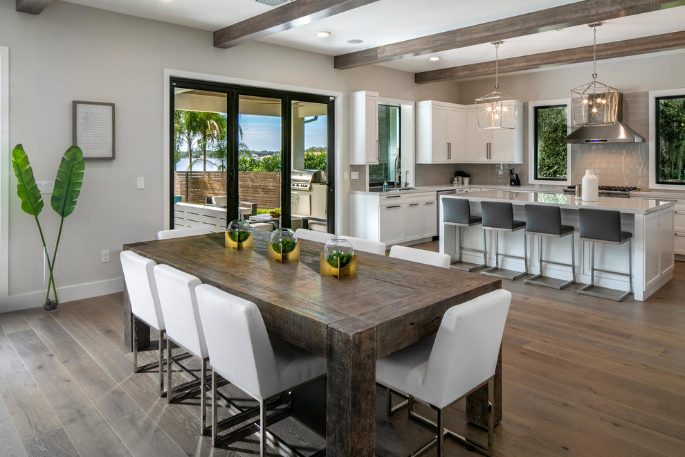 This is an example of an expansive modern u-shaped kitchen/diner in Tampa with a submerged sink, shaker cabinets, white cabinets, engineered stone countertops, grey splashback, glass tiled splashback, stainless steel appliances, medium hardwood flooring, an island, brown floors and grey worktops.