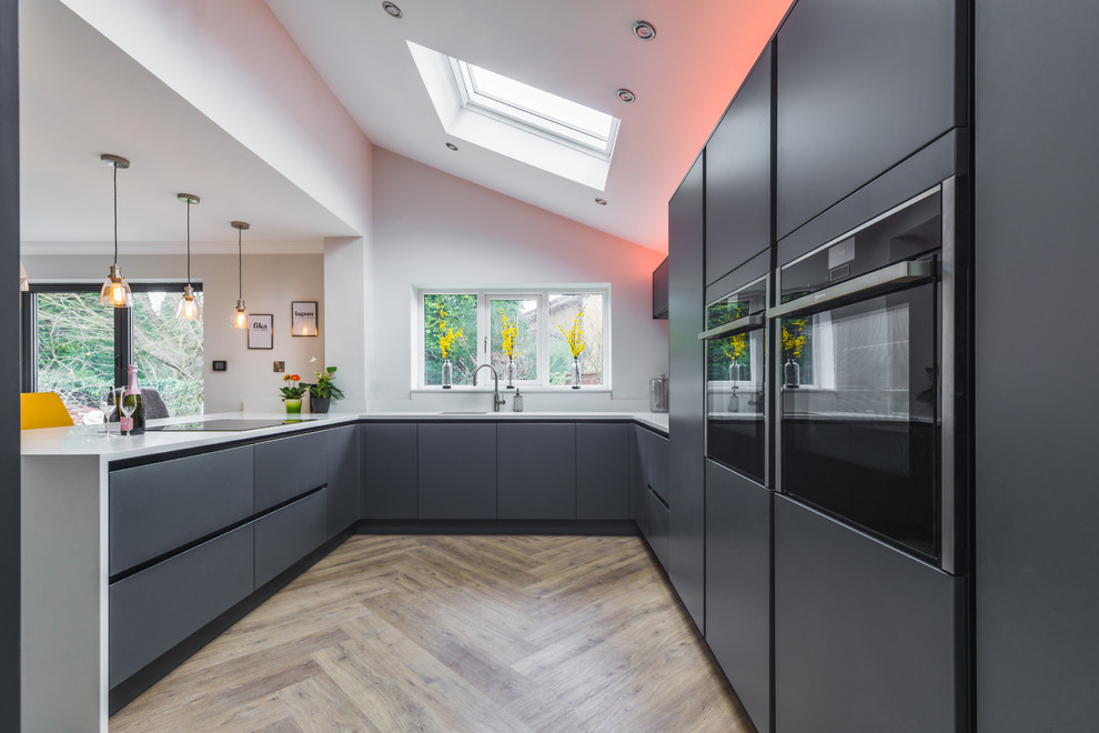 Inspiration for a scandinavian u-shaped kitchen in Cheshire with a submerged sink, flat-panel cabinets, grey cabinets, black appliances, medium hardwood flooring, a breakfast bar and white worktops.