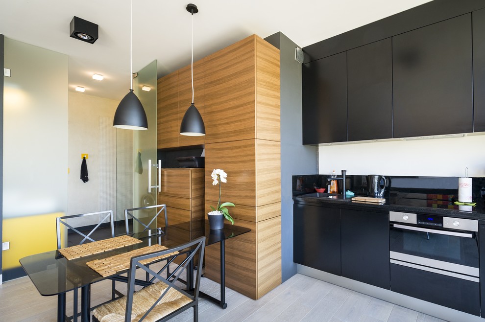Minimalist eat-in kitchen photo in Las Vegas with a drop-in sink, flat-panel cabinets, black cabinets, black backsplash and paneled appliances