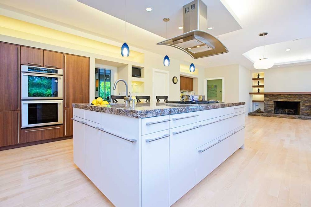 This is an example of a large contemporary u-shaped open plan kitchen in San Francisco with a submerged sink, flat-panel cabinets, white cabinets, granite worktops, white splashback, stainless steel appliances, light hardwood flooring, an island, beige floors and multicoloured worktops.