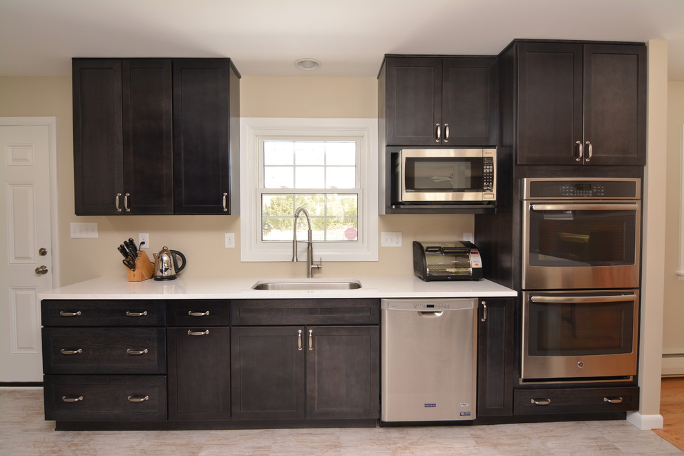 Mid-sized transitional single-wall vinyl floor eat-in kitchen photo in Baltimore with a single-bowl sink, flat-panel cabinets, black cabinets, solid surface countertops, stainless steel appliances and beige backsplash