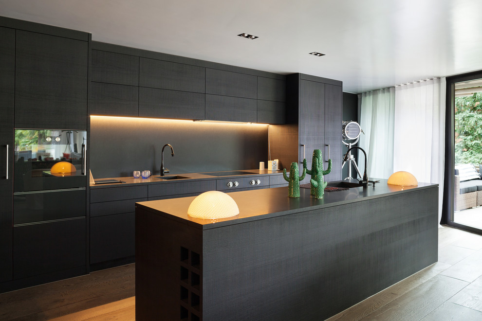 Inredning av ett modernt mellanstort svart linjärt svart kök och matrum, med en undermonterad diskho, släta luckor, svarta skåp, laminatbänkskiva, svart stänkskydd, stänkskydd i trä, svarta vitvaror, mellanmörkt trägolv, en köksö och flerfärgat golv